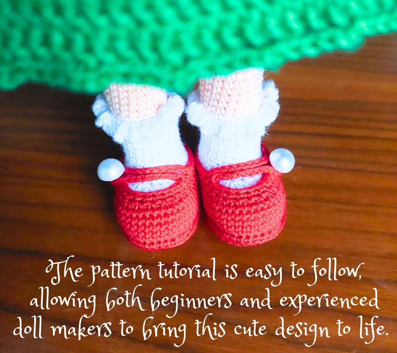 May include: A pair of red crocheted doll shoes with white trim and pearl accents. The shoes are on a wooden surface.