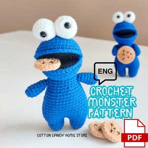 May include: Two blue crocheted monster dolls with large white eyes and black pupils. One doll has a tan cookie in its mouth, and the other has a tan cookie on its chest. Text reads: ENG CROCHET MONSTER PATTERN, COTTON CANDY HOME STORE, and PDF.