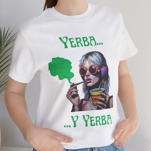 May include: White t-shirt with a green and purple illustration of a woman wearing sunglasses and headphones, smoking a cigarette and holding a can of Yerba Mate. The text "YERBA... ...Y YERBA" is printed on the shirt.