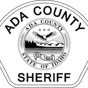 Può includere: Distintivo in bianco e nero con il testo "ADA COUNTY SHERIFF" in grassetto. Il distintivo presenta un sigillo con il testo "ADA COUNTY STATE OF IDAHO EST. 1864" e un'aquila calva con tre stelle sopra.