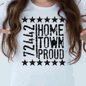 以下が含まれることがあります： 「72472 Hometown Proud」の文字が黒の擦れたフォントでプリントされた白いTシャツ。黒い星の形で縁取られています。カジュアルウェアです。