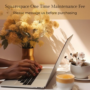 May include: A person's hands typing on a silver laptop computer with a white background. The laptop is open and the screen is visible. There are flowers in a gold vase and a cup of coffee on the table.