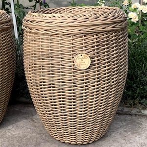 Può includere: Un grande cesto ovale in vimini di colore marrone naturale. Il cesto ha un motivo intrecciato e un'etichetta che dice "Garden & Home Decor".