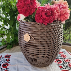 Op de afbeelding: Een bruine rieten vaas met een houten label met de tekst "Garden & Home Decor" is gevuld met roze en rode pioenen.