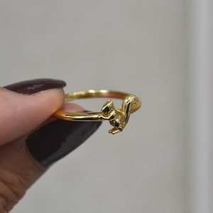May include: A gold ring with a detailed squirrel design. The ring has a thin band with a three-dimensional squirrel as a prominent feature. The squirrel is in a dynamic pose, adding a playful touch to the jewellery.
