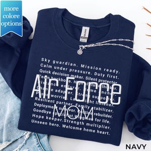 May include: A navy blue crewneck sweatshirt featuring white text that reads Air Force Mom, surrounded by descriptive phrases like Sky guardian, Mission ready, Calm under pressure, Duty first, Silent protector, and Unseen hero, Welcome home heart.