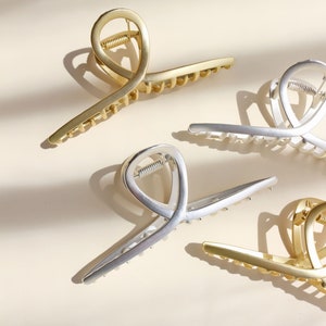 Pinzas de metal mate con forma de garra, grandes, doradas y plateadas, de fijación fuerte y con lazo giratorio.