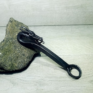 May include: A black metal bottle opener shaped like a dragon's head with a ring at the end of the handle.