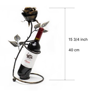 May include: A black metal wine bottle holder shaped like a rose with a bottle of red wine inside. The holder is 15 3/4 inches tall.