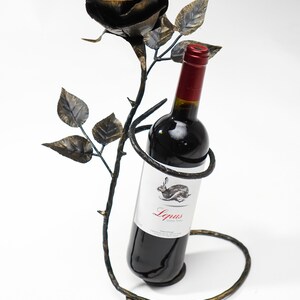 May include: A black metal wine bottle holder shaped like a rose with a bottle of red wine inside. The bottle label says "Lepus Argentina".