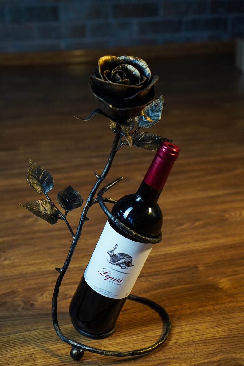 May include: A black metal wine bottle holder shaped like a rose with a bottle of red wine inside. The label on the bottle reads "Lupus Vino Tinto".