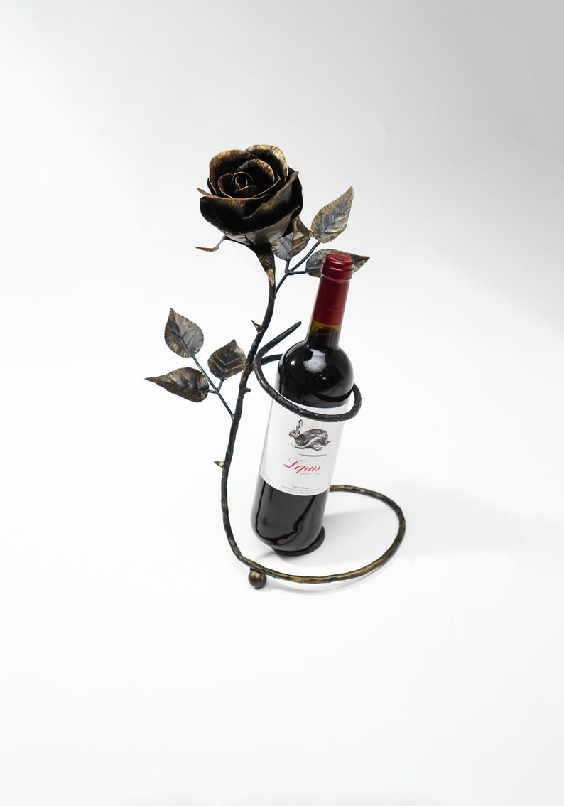 May include: A black metal wine bottle holder shaped like a rose with a bottle of red wine inside. The label on the bottle reads "Lygus Wine Co."