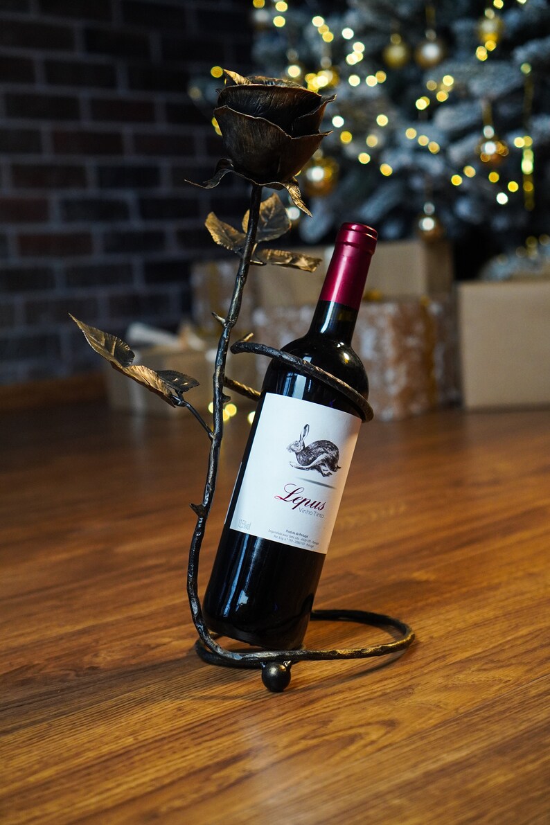 May include: A black metal wine bottle holder shaped like a rose with a bottle of red wine inside. The label on the bottle reads "Lepus Vino Tinto".