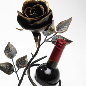 May include: A black metal wine bottle holder shaped like a rose with a bottle of red wine inside. The bottle label says "Lepus Vinho Tinto".