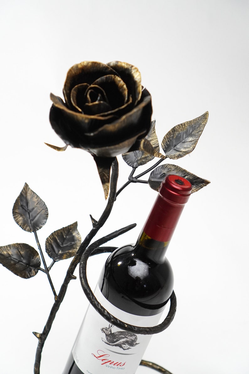 May include: A black metal wine bottle holder shaped like a rose with a bottle of red wine inside. The bottle label says "Lepus Vinho Tinto".