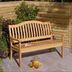 May include: A light brown wooden garden bench with a slatted back and seat, and armrests. A book rests on the seat. A tray with drinks sits in front of the bench. The bench is outdoors.