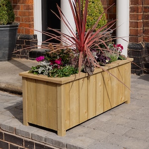 May include: A wooden planter box with a natural finish, filled with a variety of plants, including a red-leaved plant, pink flowers, and green foliage.
