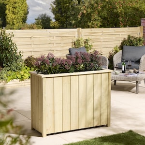 May include: A large, rectangular wooden planter filled with purple flowering plants. The light-coloured wood has vertical planks. The planter is on a patio with outdoor furniture and a wooden fence in the background.