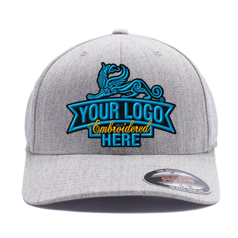 Może przedstawiać: Szara czapka bejsbolowa z zakrzywionym daszkiem. Czapka posiada niestandardowe logo z napisem "YOUR LOGO Embroidered HERE" w kolorze niebieskim i złotym. Czarno-biała naklejka znajduje się na daszku.