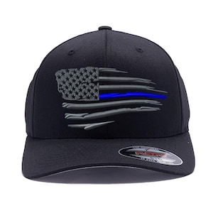 May include: Black baseball cap with a gray and blue American flag design. The flag has a thin blue line across the middle. The cap has a Flexfit logo on the back.