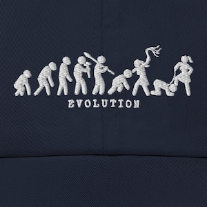 Peut inclure: Casquette de baseball bleu marine avec un motif brodé blanc représentant l'évolution d'une personne. Le mot "EVOLUTION" est brodé en dessous des figures. La casquette a une visière incurvée et une fermeture à sangle en tissu.