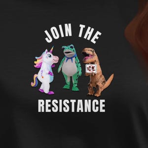 May include: Black t-shirt with the text "JOIN THE RESISTANCE" above a graphic of a unicorn, frog, and dinosaur. The unicorn is white and purple, the frog is green, and the dinosaur is brown.