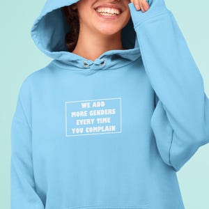 May include: A light blue hoodie with a white graphic that says "We add more genders every time you complain".
