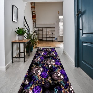 May include: A black and purple runner rug with a skull and floral design. The rug is placed in a hallway with a white wall and a wooden floor.