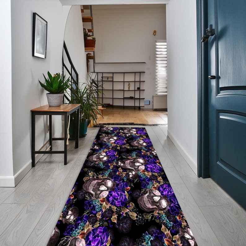 May include: A black and purple runner rug with a skull and floral design. The rug is placed in a hallway with a white wall and a wooden floor.