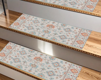 May include: Three stair treads with a cream-colored, floral patterned design. The treads feature a central floral motif in shades of orange and blue, framed by a border with similar colors. The treads are placed on wooden stairs.