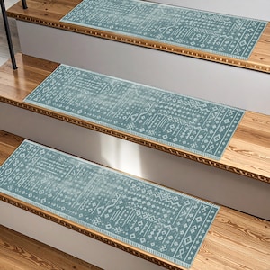 May include: Three stair treads with a teal and white geometric pattern are installed on wooden stairs. The treads have a rectangular shape and a border of white stitching. The stairs are made of light brown wood.