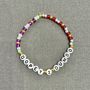 May include: A colorful beaded bracelet with the words "DOPEY 2 DUMBO" spelled out in white beads.