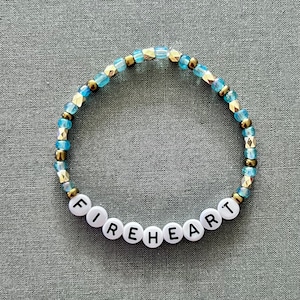 May include: A blue and gold beaded bracelet with the word "FIREHEART" spelled out in white beads.
