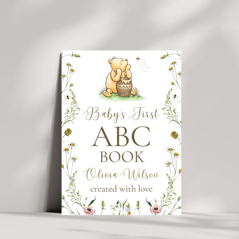 K&ouml;nnte beinhalten: Eine wei&szlig;e Karte mit einer Winnie-the-Pooh-Illustration und gr&uuml;nem floralen Rand. Der Text lautet "Baby's First ABC Book Olivia Wilson created with love."