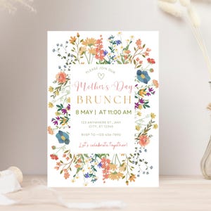 May include: A floral-themed invitation for a Mother's Day brunch. The invitation features a wreath of colorful flowers and greenery with the text "Please join our Mother's Day Brunch" in pink and gold lettering. The date and time of the brunch are listed as "8 May | at 11:00 AM" along with the address and RSVP information. The invitation concludes with the phrase "Let's celebrate together!"