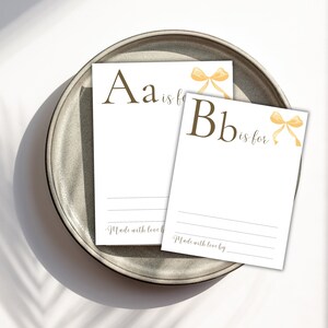 K&ouml;nnte beinhalten: Zwei wei&szlig;e Karten mit braunen Buchstaben und gelben Schleifen. Die erste Karte sagt "Aa ist f&uuml;r" und die zweite Karte sagt "Bb ist f&uuml;r". Beide Karten haben den Text "Made with love by" unten.