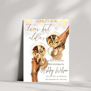 May include: A white invitation card with a gold and pink design. The card features a graphic of two hands holding champagne flutes. The text on the card reads "Ashley is a Tini bit older" and includes details for a 30th birthday party.