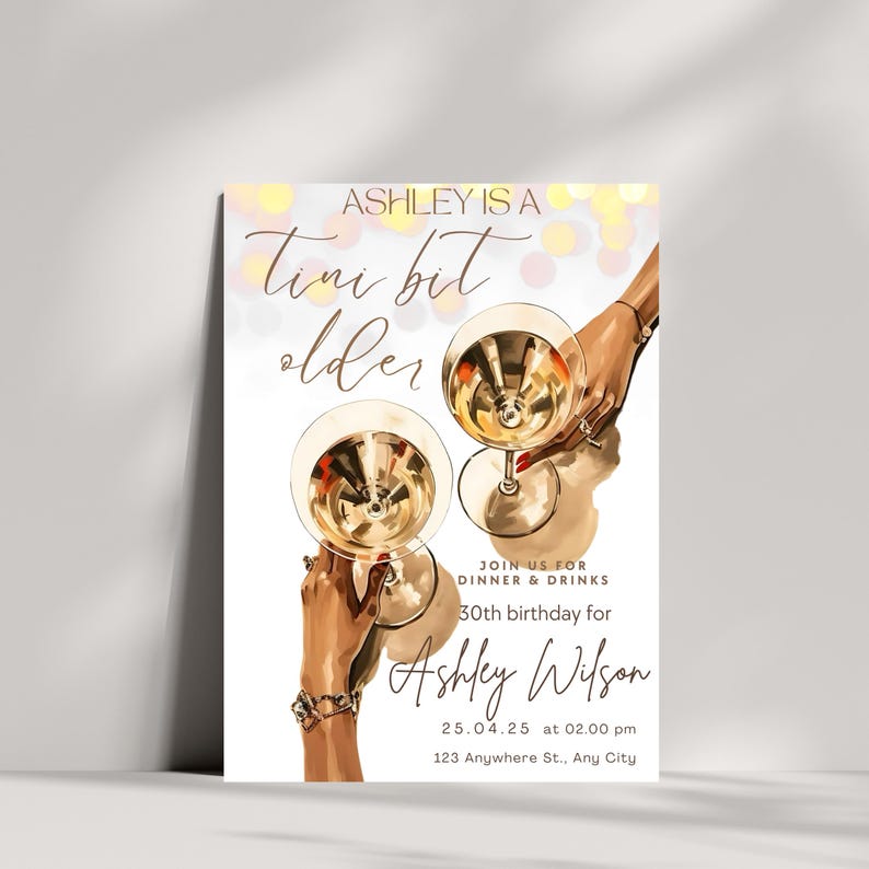 May include: A white invitation card with a gold and pink design. The card features a graphic of two hands holding champagne flutes. The text on the card reads "Ashley is a Tini bit older" and includes details for a 30th birthday party.