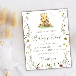 K&ouml;nnte beinhalten: Ein Babyparty-Spielschild im Winnie-the-Pooh-Stil mit floralem Rand. Das Schild lautet "Bitte hilf uns, Babys erstes zu f&auml;rben". Die Anweisungen sind, einen Buchstaben auszuw&auml;hlen, etwas zu zeichnen, das mit diesem Buchstaben beginnt, und deinen Namen zu unterschreiben.