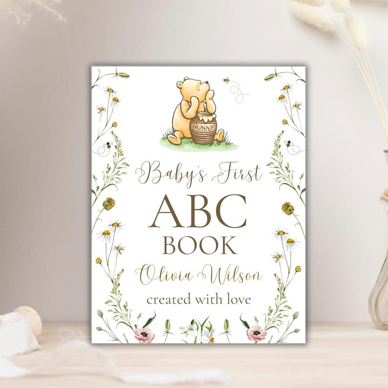 K&ouml;nnte beinhalten: Ein wei&szlig;er Hintergrund mit einer Illustration von Winnie Puuh, der einen Honigtopf h&auml;lt. Der Text lautet "Baby's First ABC Book Olivia Wilson created with love".