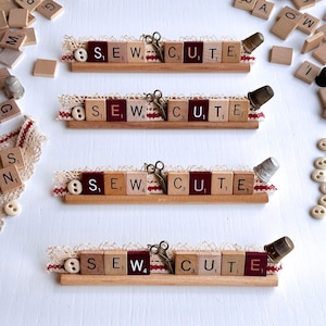 May include: Four wooden signs with the words "SEW CUTE" spelled out using letter tiles. Each sign has a small spool of thread, a thimble, and a pair of scissors.
