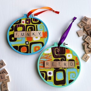 May include: Two round, blue and turquoise, fabric-covered ornaments with a geometric pattern. Each ornament has a word spelled out with letter tiles. The first ornament says "FUNKY" and the second ornament says "RETRO".