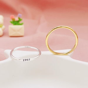 Peut inclure: Deux bagues simples en argent et en or sur une surface blanche. La bague en argent porte l'année 1997 gravée.