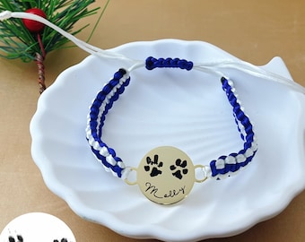 May include: A blue and white braided bracelet with a gold charm featuring two paw prints and the name "Molly" engraved on it.