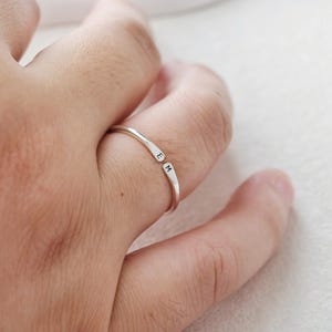 May include: A silver-coloured open band ring featuring two tapered ends. Each end is stamped with a single black letter, specifically the letter E on one side and the letter M on the other, creating a personalised look on the thin metal band.