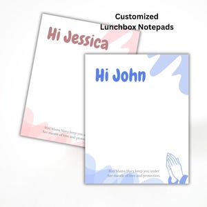May include: Two customized lunchbox notepads. One notepad has "Hi Jessica" in pink, the other has "Hi John" in blue. Both have a decorative design and a prayer. Text reads "May Mama Mary keep you under her mantle of love and protection."