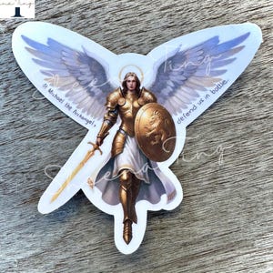 Könnte beinhalten: Ein Aufkleber mit dem Erzengel Michael, dargestellt in goldener Rüstung, der ein Schwert und einen Schild hält. Der Schild zeigt ein Löwenemblem. Der Engel hat große, detaillierte Flügel. Text enthält "St. Michael the Archangel" und "defend us in battle."