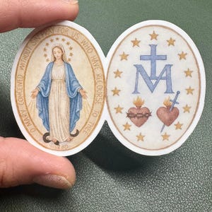 May include: Oval sticker with two designs. One side shows a woman in a blue robe with text: "O Mary conceived without sin pray for us who have recourse to thee 1830." The other side features a cross, the letter "M", two hearts, and stars.