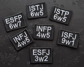 May include: Seven black embroidered patches with white text, each displaying a four-letter personality type abbreviation and a number combination. The patches are arranged on a dark, textured surface.