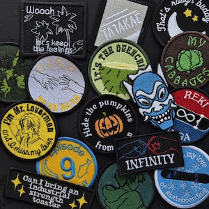 May include: A selection of embroidered patches with diverse designs and text. The patches display images of a palm tree, hands, a pumpkin, a blue mask, and text such as "Woooh", "Infinity", and "Episode 9". The patches are in various colours, including black, yellow, and blue.